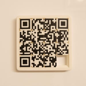 May include: A white puzzle with a grid of black and white QR code tiles. One tile is missing from the bottom right corner. The puzzle is set against a white background.