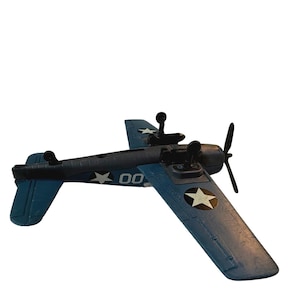 May include: A blue toy airplane with white star and number 00 decals on the wings and fuselage. The propeller is black, and the plane has a detailed cockpit and tail assembly. The toy is likely a collectible or a model.