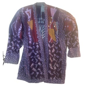 May include: A long-sleeved jacket featuring a patchwork design in shades of purple, maroon, and blue. The garment displays various geometric patterns, including zigzags, dots, and triangles, with a central open front and a structured collar.