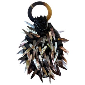Peut inclure: Un sac à main noir doté d'une poignée circulaire au motif marbré brun et beige. L'extérieur est recouvert de nombreuses pièces allongées et irisées ressemblant à des coquillages dans des tons bruns, gris et blancs, créant un aspect texturé.