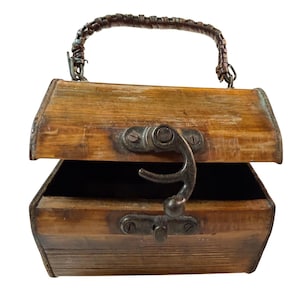 May include: A vintage wooden handbag with a hinged lid and a braided handle. The bag features a metal clasp and hardware, with a distressed finish. The interior is dark, contrasting with the light brown wood. The bag is designed to be carried by the handle.