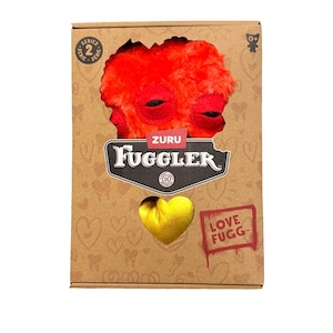 Könnte beinhalten: Ein Fuggler-Plüschtier in einer Pappschachtel. Das Plüschtier ist rot mit schwarzen Augen und einem Mund. Die Schachtel hat einen herzförmigen Ausschnitt, der ein goldenes Herz freilegt. Auf der Schachtel steht "ZURU Fuggler" und "LOVE FUGG".