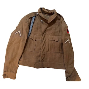 May include: A brown military jacket with two front pockets, a collar, and button closures. The jacket features a light blue shoulder strap and a patch on the sleeve. The jacket has two chevrons on the sleeves.