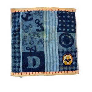 May include: Square blue and white patterned towel with a red border. The towel features anchors, the letter "D", and a Donald Duck patch. The design includes stripes and polka dots.