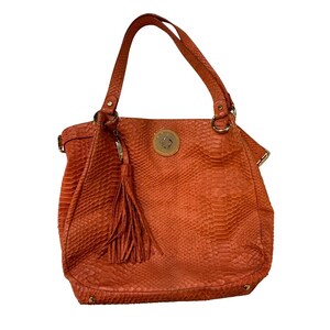 May include: Orange handbag with a textured snakeskin pattern. The bag has a top handle, a long tassel, and gold-colored hardware. The bag is a tote style.