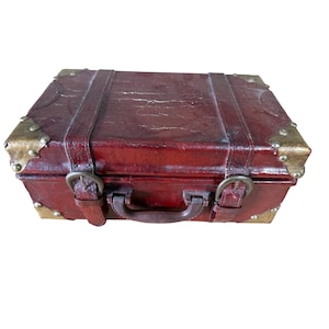 May include: A vintage burgundy leather suitcase with brass corner protectors and accents. The suitcase has a handle and two leather straps with buckles. The exterior shows signs of wear, adding to its antique charm.