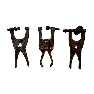 May include: Three vintage metal hand tools with a dark, weathered, and rusted finish. Each tool features a U-shaped head with an adjustable screw mechanism and a pair of hinged handles, showing signs of age and heavy industrial use.