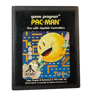 以下が含まれることがあります： 黒いAtari Pac-Manビデオゲームカートリッジ。ラベルには、ピンクの手、幽霊、Atariのロゴが付いた黄色のPac-Manキャラクターが描かれています。「game program PAC-MAN」と「Use with Joystick Controllers」というテキストが含まれています。
