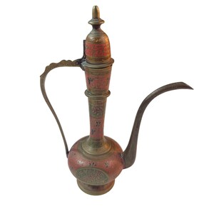 May include: An antique brass water pitcher with a long spout and ornate handle. The pitcher features red and gold floral designs and a hinged lid. The overall design is reminiscent of Middle Eastern or Indian craftsmanship.