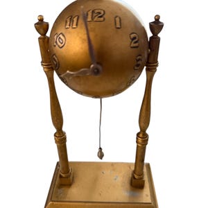 May include: A vintage brass desk clock with a spherical clock face. The clock has a gold finish, Roman numerals, and decorative supports. The clock face is round, and the hands are black. The clock sits on a rectangular base.