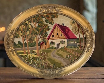 May include: Oval framed needlepoint art featuring a rural landscape with a house, trees, and a winding road. The house has a red roof and is surrounded by greenery. The frame is gold-colored with ornate detailing.