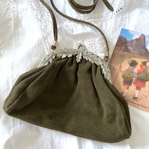 Può includere: Una borsa in pelle scamosciata verde scuro con una chiusura argentata con un design a foglia di quercia. La borsa ha una tracolla lunga ed è chiusa.