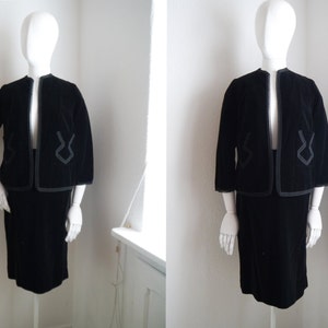 May include: A black velvet skirt suit with a jacket featuring a geometric design. The jacket has a collar and three-quarter sleeves. The skirt is knee-length.