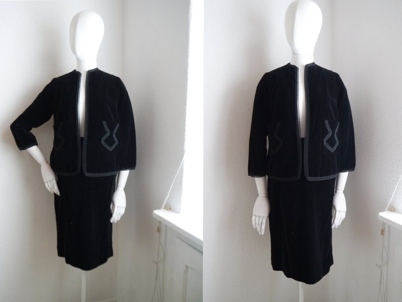 May include: A black velvet skirt suit with a jacket featuring a geometric design. The jacket has a collar and three-quarter sleeves. The skirt is knee-length.
