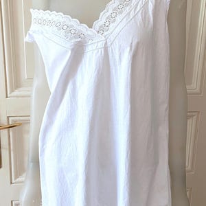 May include: A white, sleeveless nightgown with a V-neckline. The neckline and shoulders are trimmed with delicate white lace. The nightgown is displayed on a mannequin and has a simple, elegant design.