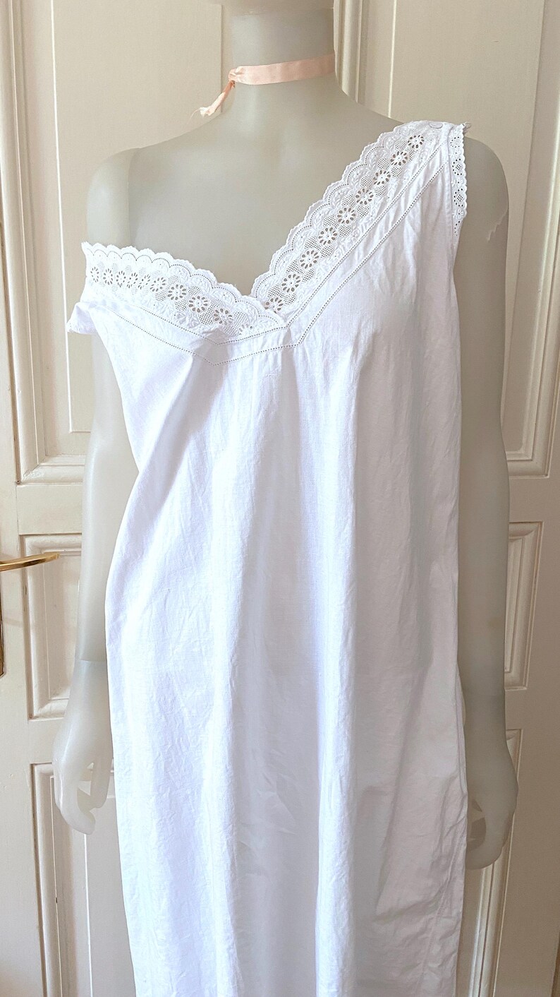 May include: A white, sleeveless nightgown with a V-neckline. The neckline and shoulders are trimmed with delicate white lace. The nightgown is displayed on a mannequin and has a simple, elegant design.