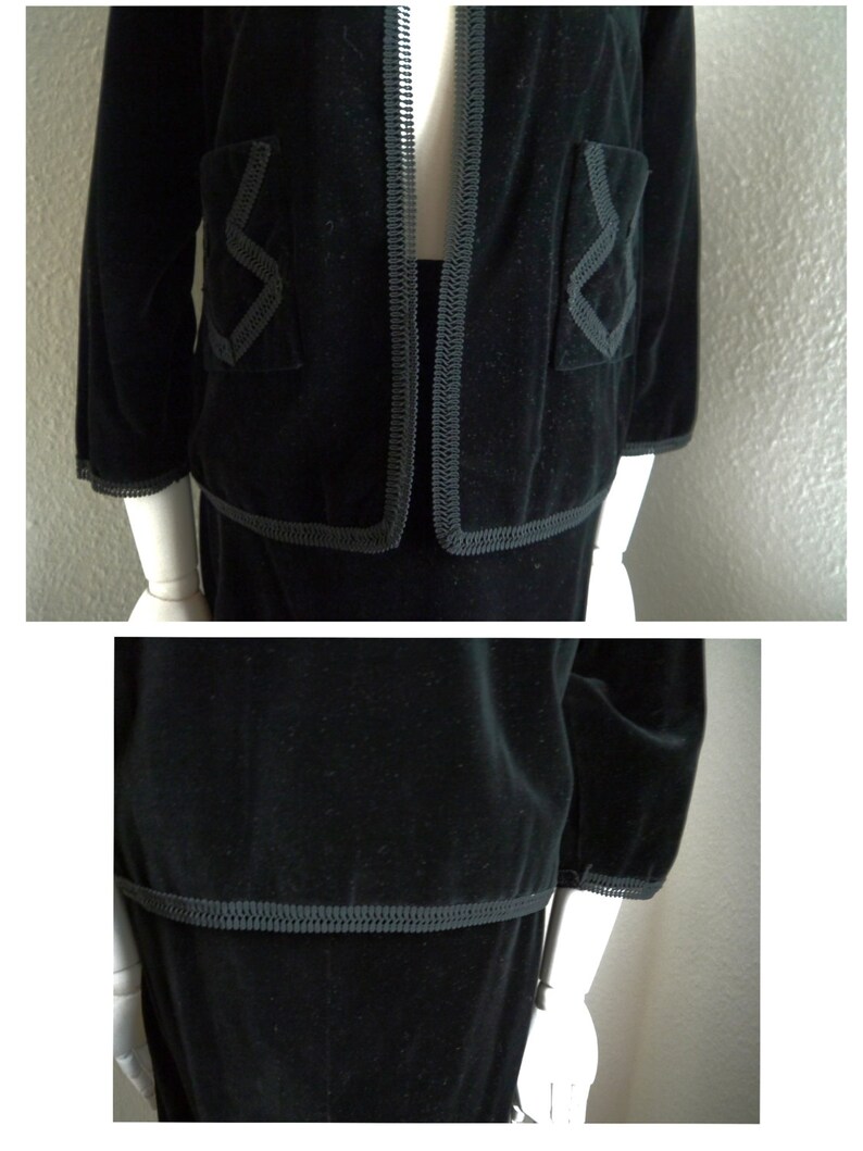 May include: A black velvet suit with a trim of gray piping. The jacket has a collar and long sleeves. The skirt is knee-length.