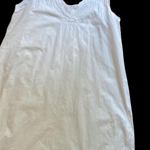 May include: A white sleeveless nightgown with a V-neckline and delicate lace trim. The fabric appears to be lightweight and slightly textured. The garment is likely vintage or inspired by vintage styles.