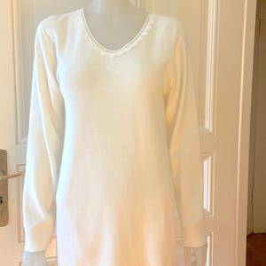 Op de afbeelding: Witte longsleeve met een kanten randje rond de hals.