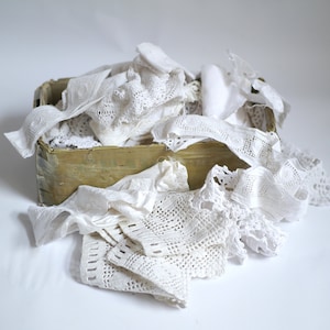 Può includere: Una scatola di legno piena di pizzo bianco e ritagli di stoffa.