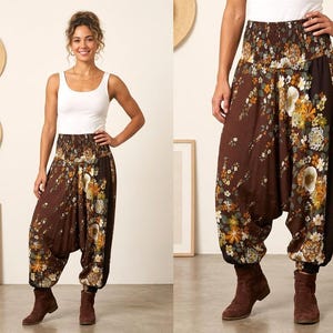 May include: Brown harem pants with a floral pattern in shades of yellow, orange, and white. The pants have a gathered elastic waistband and cuffs. The model is wearing a white tank top and brown boots.