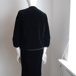 May include: A black velvet dress with a matching jacket. The dress has a straight skirt and the jacket has a slightly puffed sleeve.