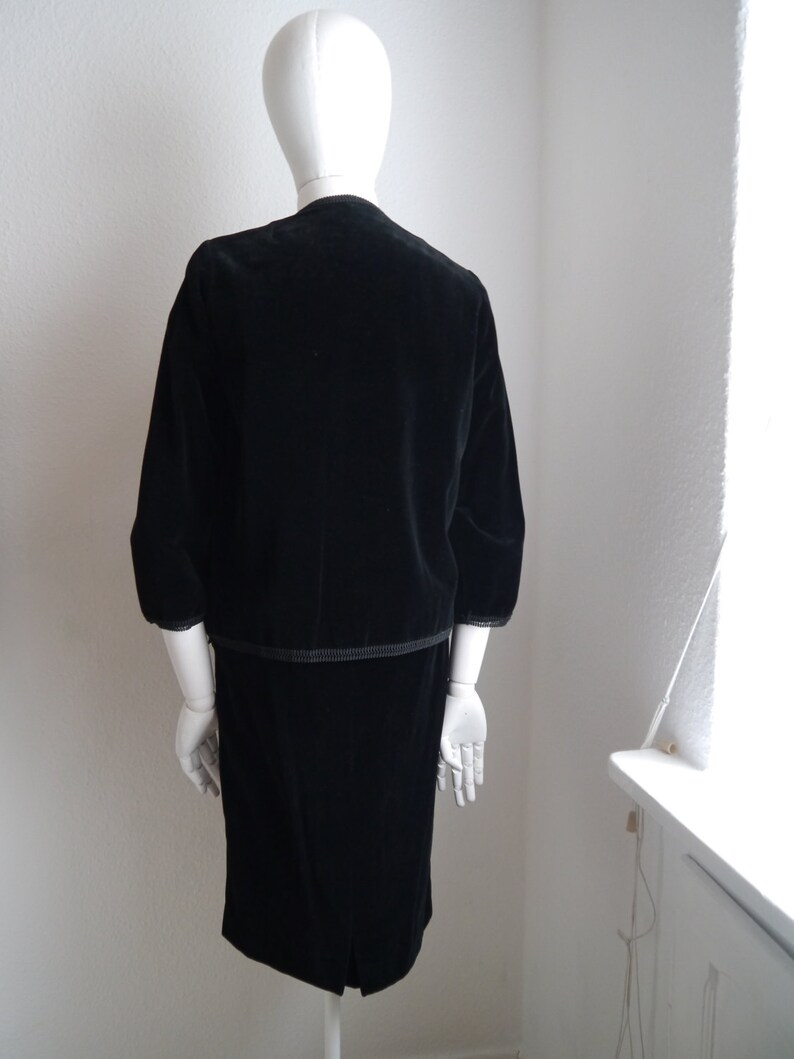 May include: A black velvet dress with a matching jacket. The dress has a straight skirt and the jacket has a slightly puffed sleeve.