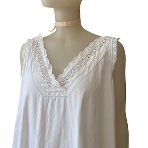 May include: A white sleeveless nightgown with a V-neckline. The neckline and shoulders are trimmed with delicate white lace. The nightgown is displayed on a mannequin.