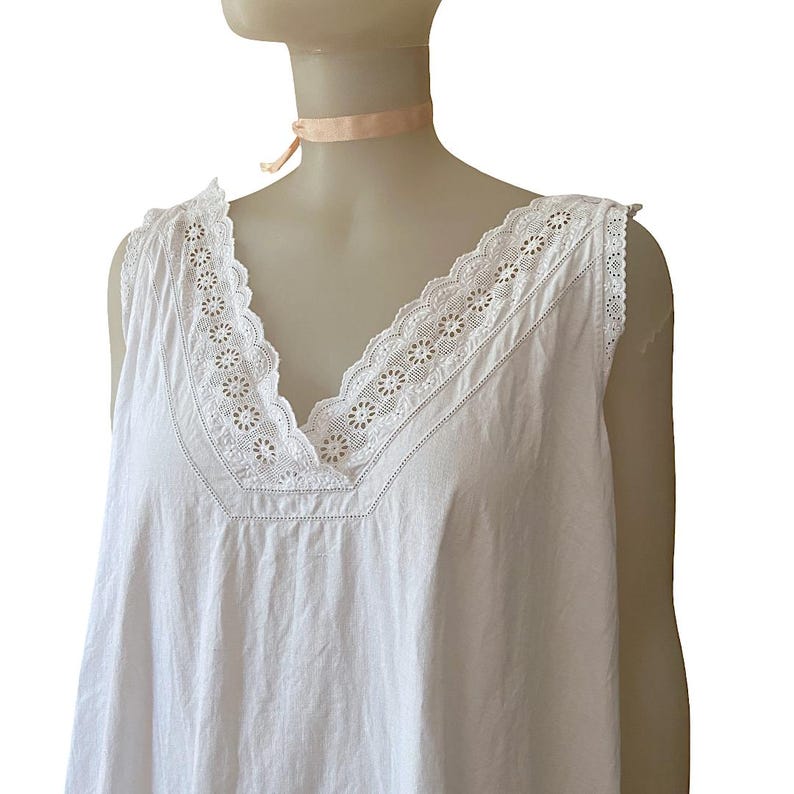 May include: A white sleeveless nightgown with a V-neckline. The neckline and shoulders are trimmed with delicate white lace. The nightgown is displayed on a mannequin.