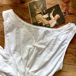 May include: A white sleeveless cotton nightgown with a lace trim around the neckline. The nightgown is folded and lying on a wooden surface.