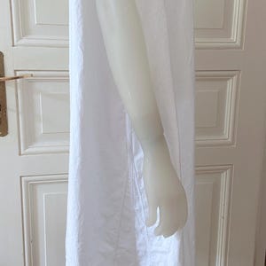 May include: A white, sleeveless dress with a simple design. The dress is made of a lightweight fabric and has a straight silhouette. The dress is displayed on a mannequin.