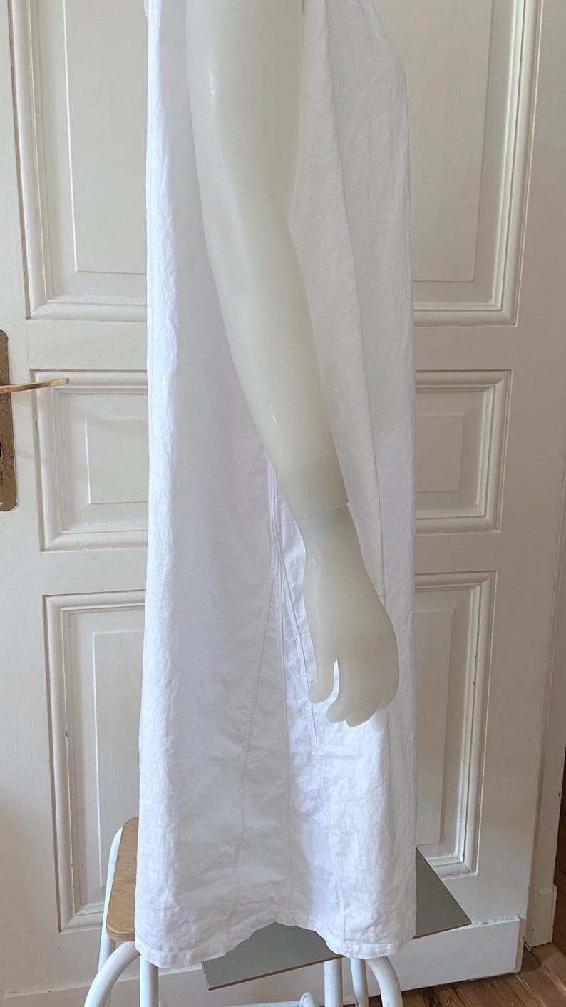 May include: A white, sleeveless dress with a simple design. The dress is made of a lightweight fabric and has a straight silhouette. The dress is displayed on a mannequin.