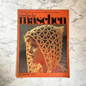 Peut inclure: Une couverture de magazine vintage représentant une femme portant une capuche en crochet. Le magazine est intitulé "modische maschen" et le texte "SOMMER 1977" est imprimé en bas.