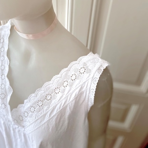 May include: White sleeveless nightgown with a V-neckline and delicate floral lace trim along the neckline and shoulders. The nightgown is displayed on a mannequin, showcasing its soft, flowing fabric and vintage design.