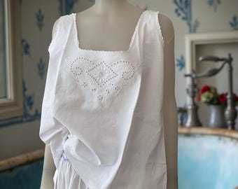 May include: White cotton camisole with a square neckline and delicate embroidered floral design. The sleeveless top features a scalloped edge and is part of a vintage-inspired lingerie set. The camisole is displayed on a mannequin.