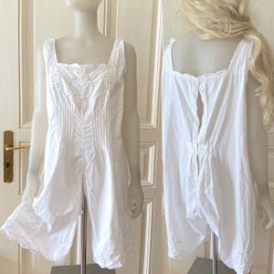 Könnte beinhalten: Weißes Unterkleid aus Baumwolle mit Spitzenbesatz und Knopfleiste im Rücken. Das Kleid hat ein tailliertes Oberteil und weite Beine.