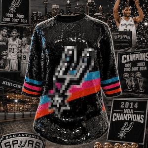 May include: A black sequined shirt featuring a pixelated San Antonio Spurs logo on the front. The design includes horizontal stripes in blue, pink, and orange across the midsection. The shirt has three-quarter length sleeves and a round neckline.