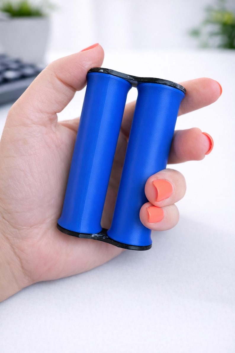 May include: A blue hand grip exerciser with black accents. The grip has two cylindrical handles connected at the base. The exerciser is held in a hand with orange nail polish.