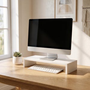 May include: A white monitor stand with a computer monitor and keyboard on a wooden desk. A small succulent plant in a white pot sits to the left of the monitor. The monitor has a black screen.