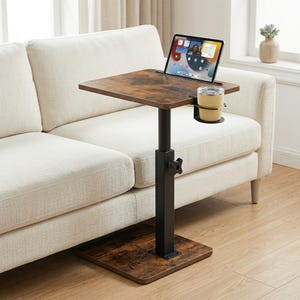May include: A brown and black adjustable laptop table with a cup holder. The table has a rectangular top with a wood grain finish. A black metal pole supports the table, and it sits on a square base. A tablet displays an app.