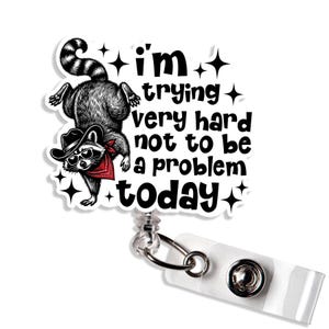 May include: A white badge reel featuring a cartoon raccoon in a cowboy hat, sunglasses, and a red bandana. The text says "I'm trying very hard not to be a problem today."