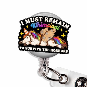 May include: A circular badge reel featuring a white unicorn with a rainbow mane and tail, wearing an orange traffic cone hat and cardboard wings. The black background includes yellow stars and the text I MUST REMAIN WHIMSICAL TO SURVIVE THE HORRORS.