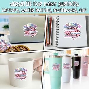 May include: A die-cut sticker featuring a pink brain illustration with the text "MY BRAIN HAS TOO MANY TABS OPEN, 4 OF THEM ARE FROZEN AND I HAVE NO IDEA WHERE THE MUSIC IS COMING FROM" applied to a laptop, a spiral notebook, a white mug, and tumblers.