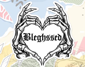 Può includere: Un adesivo bianco con la forma di un cuore formato da mani di scheletro. La parola "Blehssed" è scritta in un carattere gotico all'interno del cuore. L'adesivo ha un bordo bianco ed è posto su uno sfondo colorato.
