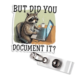 May include: A white badge reel with a cartoon raccoon working on a laptop. The raccoon is sitting in a chair with a cup of coffee on the desk. The text on the badge reel says "BUT DID YOU DOCUMENT IT?"