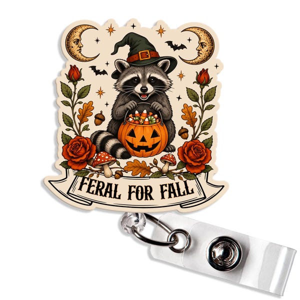 May include: A badge reel featuring a raccoon wearing a witch hat and holding a pumpkin bucket filled with candy corn. The design includes red roses, mushrooms, acorns, and crescent moons, with a banner reading FERAL FOR FALL at the bottom.