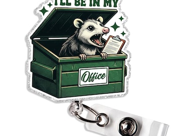 May include: A badge reel featuring a cartoon opossum in a green dumpster with the text "I'll Be In My Office." The opossum holds a clipboard. The badge reel has a white strap and a silver metal clip.
