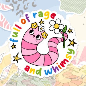 May include: A circular sticker featuring a pink worm with a smiling face, wearing a yellow flower crown, and holding a white daisy. The text "full of rage and whimsy" is written in colorful letters around the worm, accented by small yellow stars.