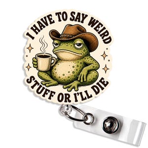 May include: A circular badge reel featuring a green frog wearing a brown cowboy hat and holding a steaming mug of coffee. The text I HAVE TO SAY WEIRD STUFF OR I'LL DIE is printed in black around the frog. The reel has a clear plastic strap.