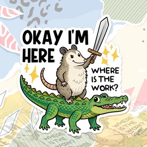 May include: A sticker with a cartoon opossum wielding a sword, atop a green alligator. The text says "OKAY I'M HERE" and "WHERE IS THE WORK?" with star accents. The design has a whimsical, cartoon style.